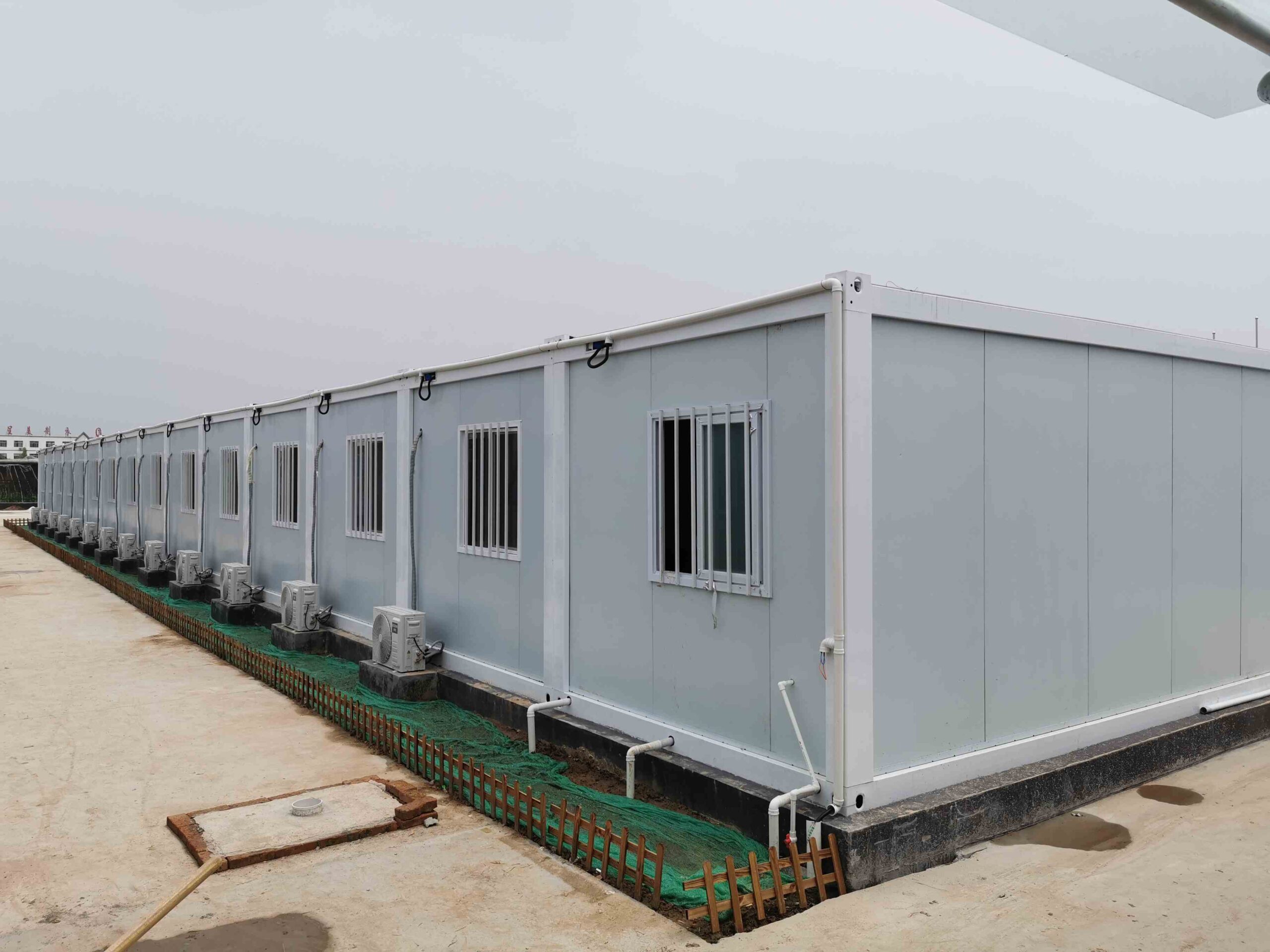 Modular detachable container house under construction with a white galvanized steel frame and sandwich panel walls for a worker dormitory project.