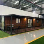 A completed expandable container house project featuring a premium wood-grain exterior finish, a large integrated front porch with black steel railings, and sliding glass doors.