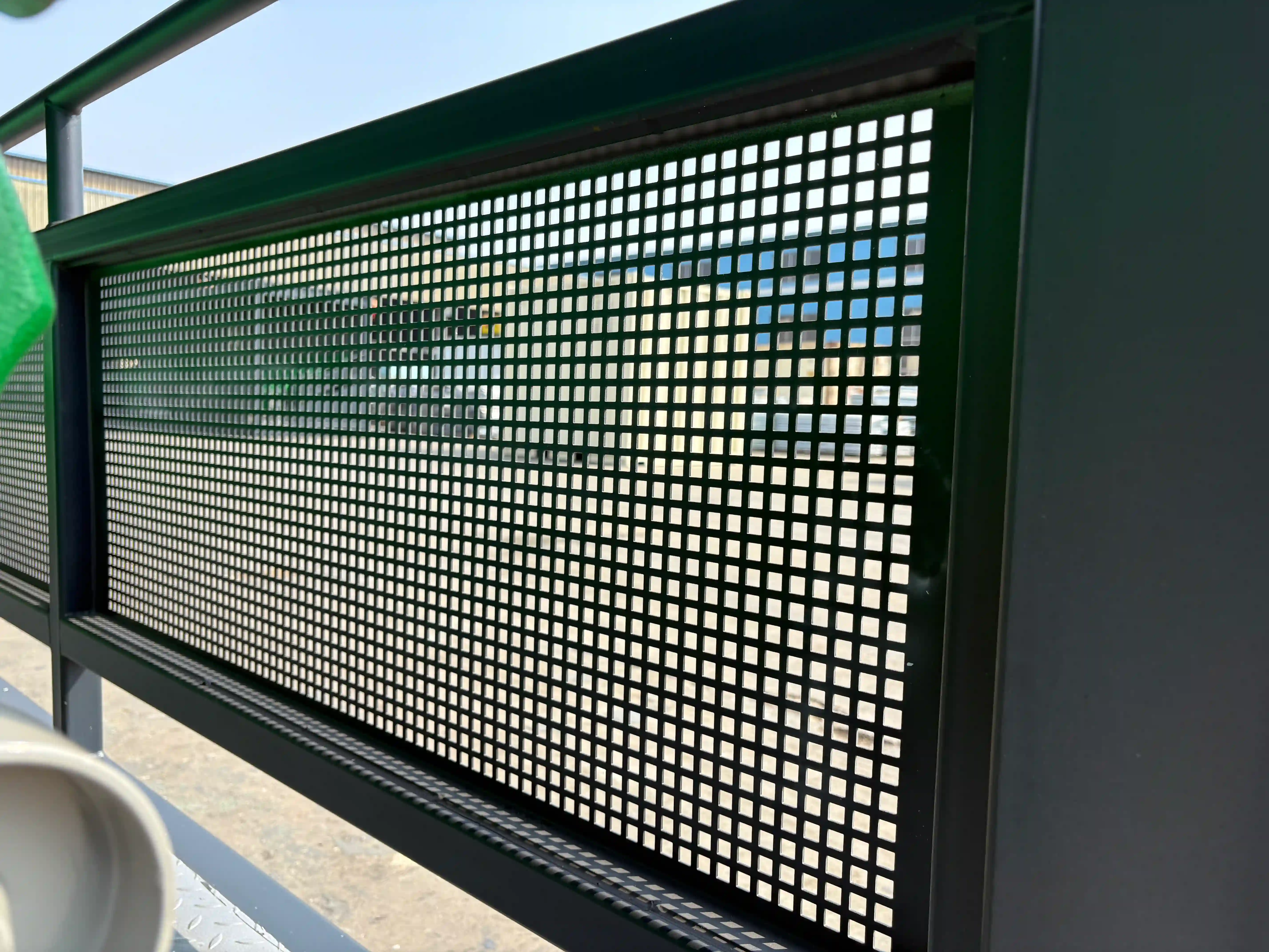 The image highlights the durable construction and safety features of a modern guardrail, combining functional perforated metal with a robust structural frame for use in spectator or industrial environments.